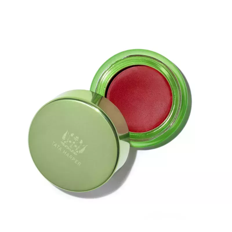 Tata Harper Cream Blush: A green jar with matching cap filled with red cream blush makeup on a white background