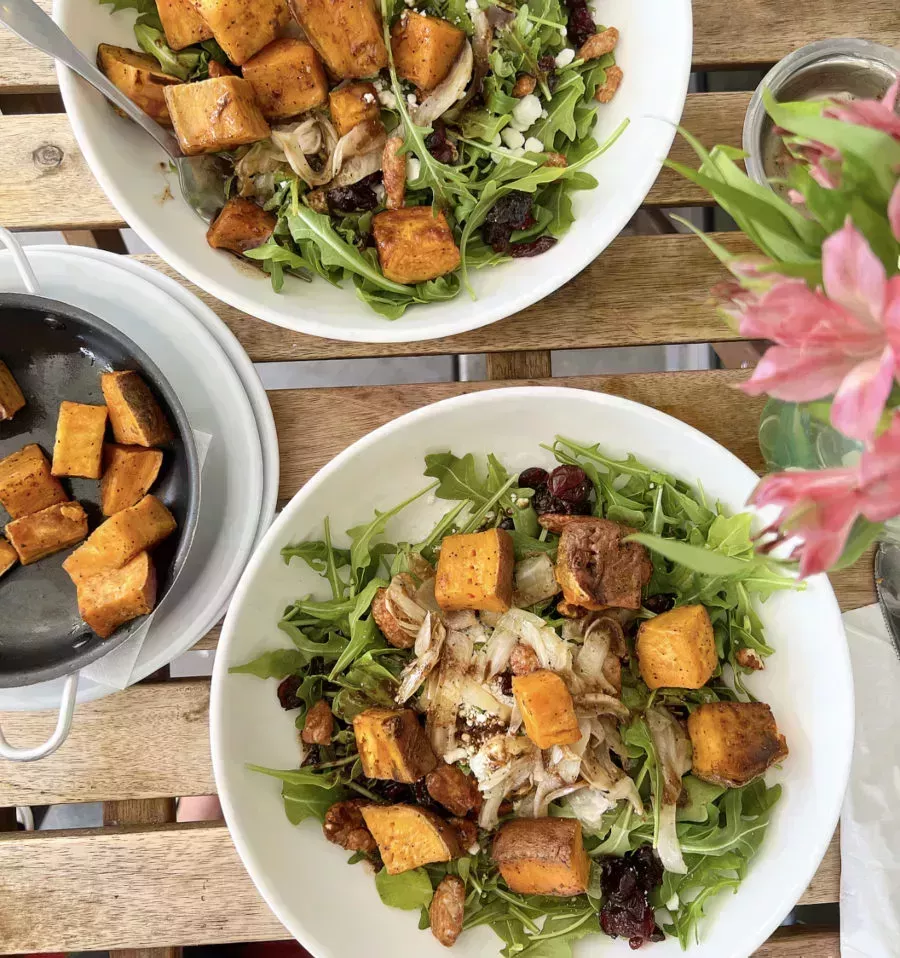two salad bowls with greens and sweet potatoes and pink flowers