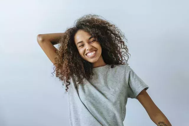 portrait of woman with afro hair smiling with white wall background