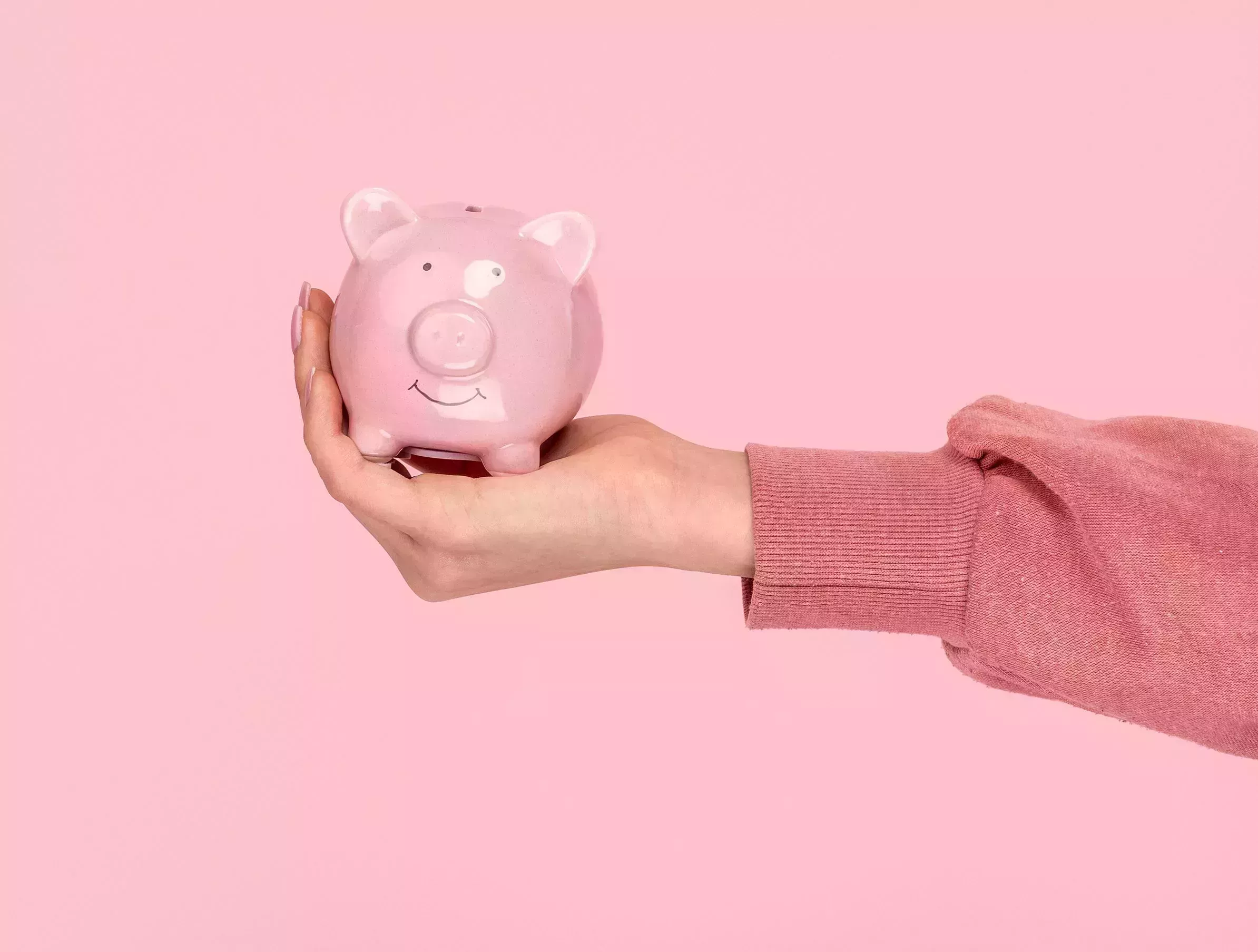 hand of female holding piggy bank while holding it on pink background