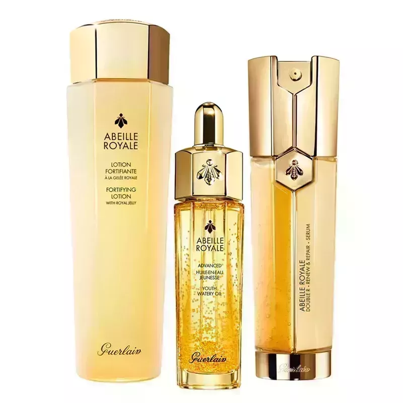 A photo of the Guerlain Abeille Royale Skin Care Bestsellers Set, including three gold-hued bottles of product from the brand, on a white background