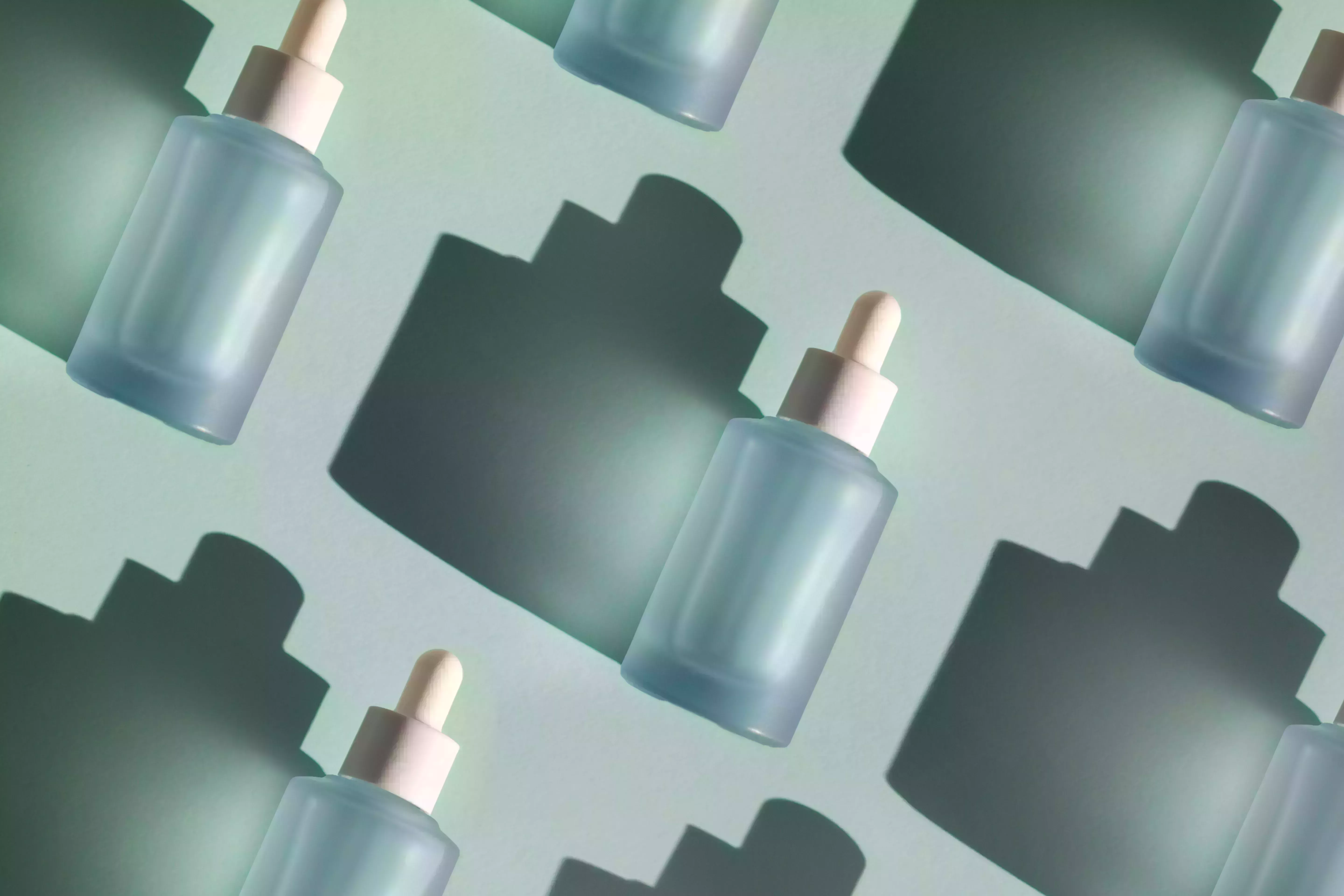 blue glass bottle with cosmetic liquid on pastel mint green background with shadow flat lay style and close up copy space for your design