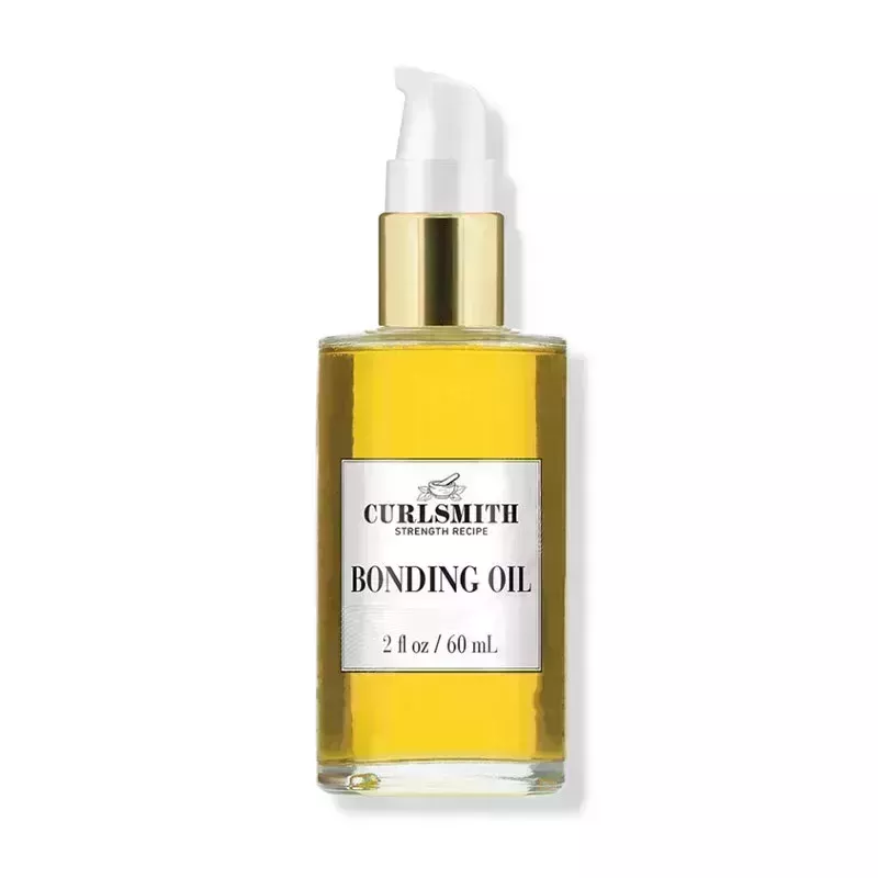 A clear glass pump bottle of the gold-hued Curlsmith Bonding Oil on a white background