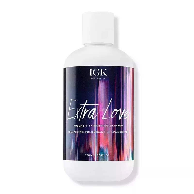 A white, black, and holographic purple bottle of the IGK Extra Love Volume & Thickening Shampoo on a white background