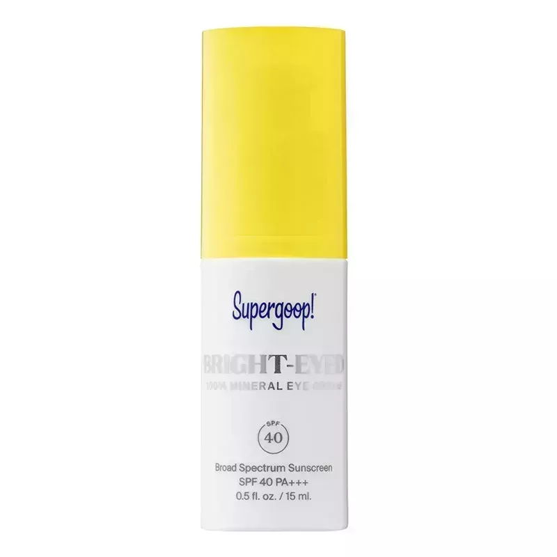 A white pump bottle with yellow cap of the Supergoop Bright-Eyed 100% Mineral Eye Cream SPF 40 on a blank background