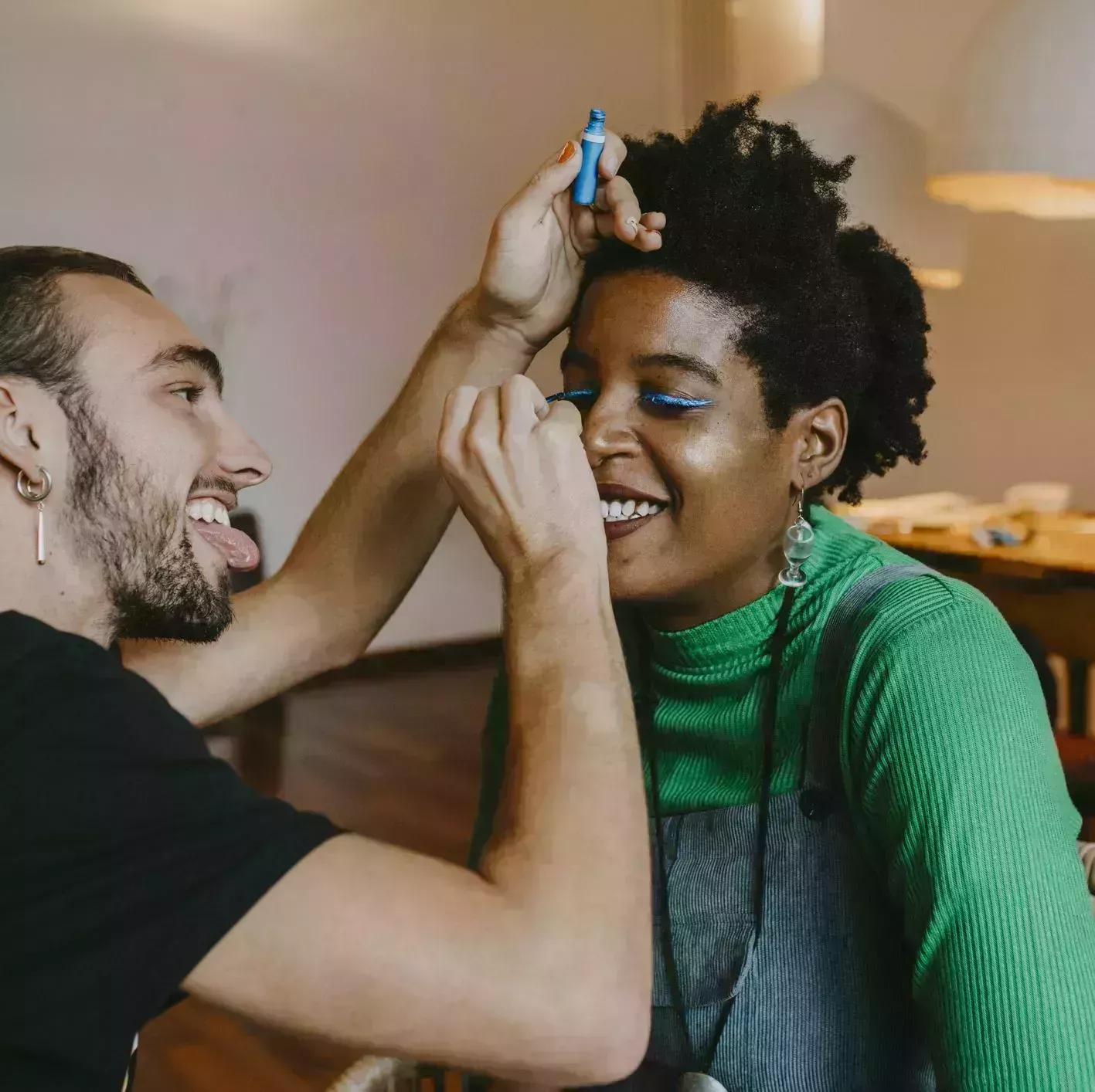 smiling man applying blue eyeliner to female friend at home