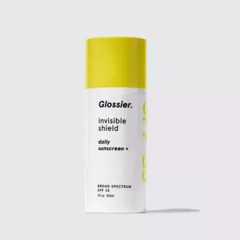 A white bottle with yellow cap of the Glossier Invisible Shield on a gray background