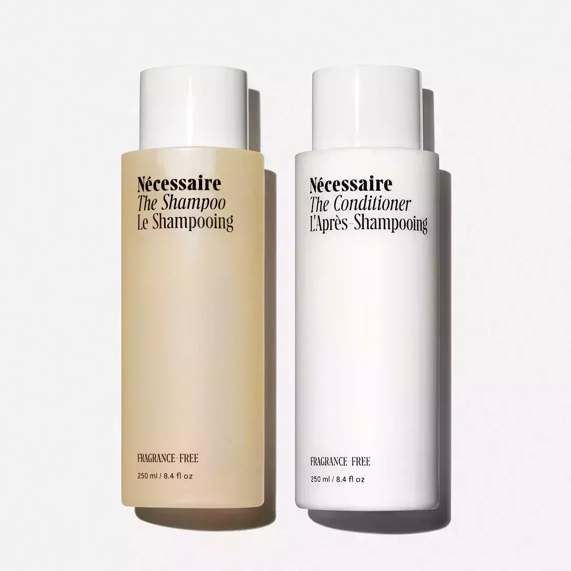 Nécessaire The Shampoo and Conditioner one translucent and one white bottle with white caps on white background