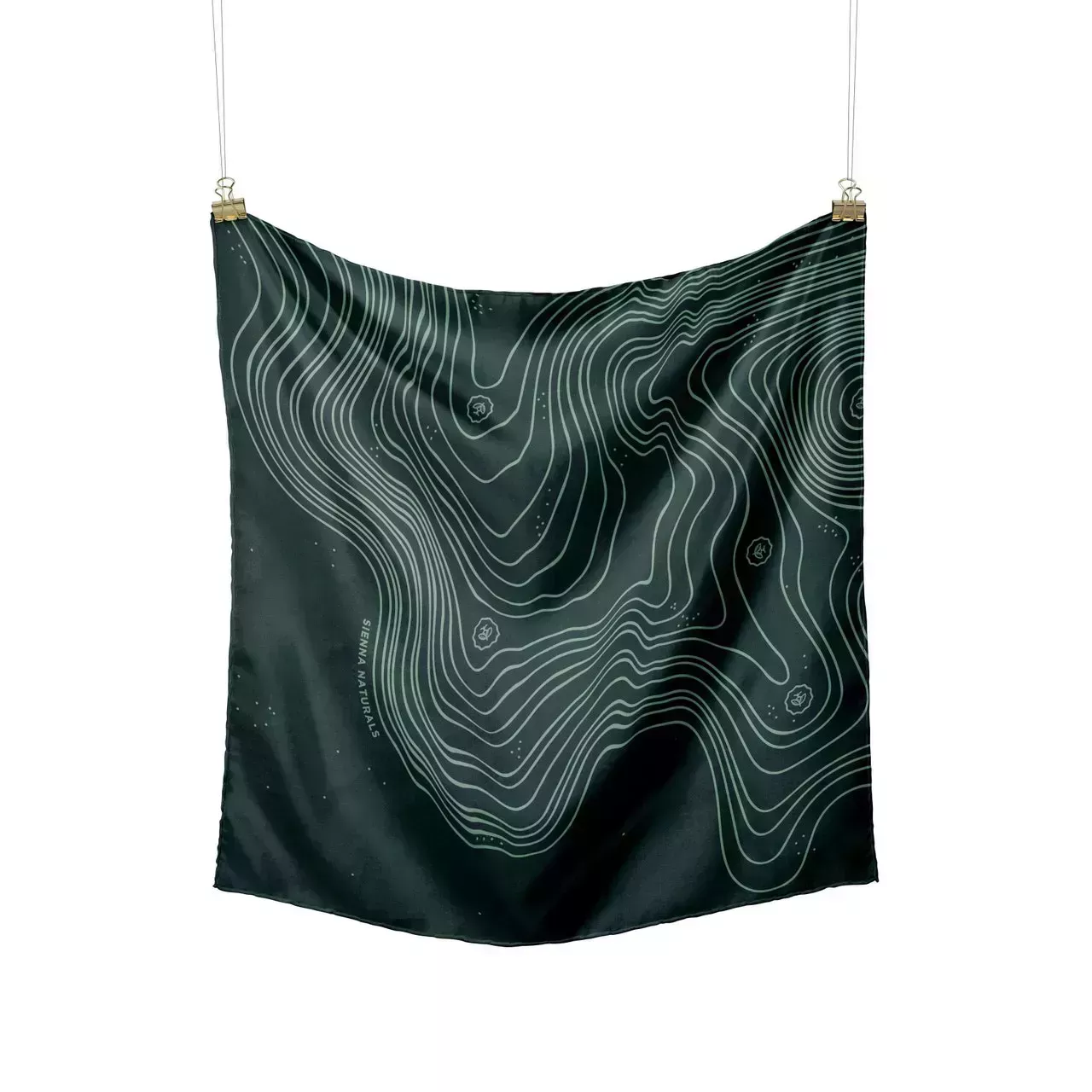 Sienna Naturals Silk Scarf dark green square scarf with light green squiggle topography design hanging from clothespins on white background