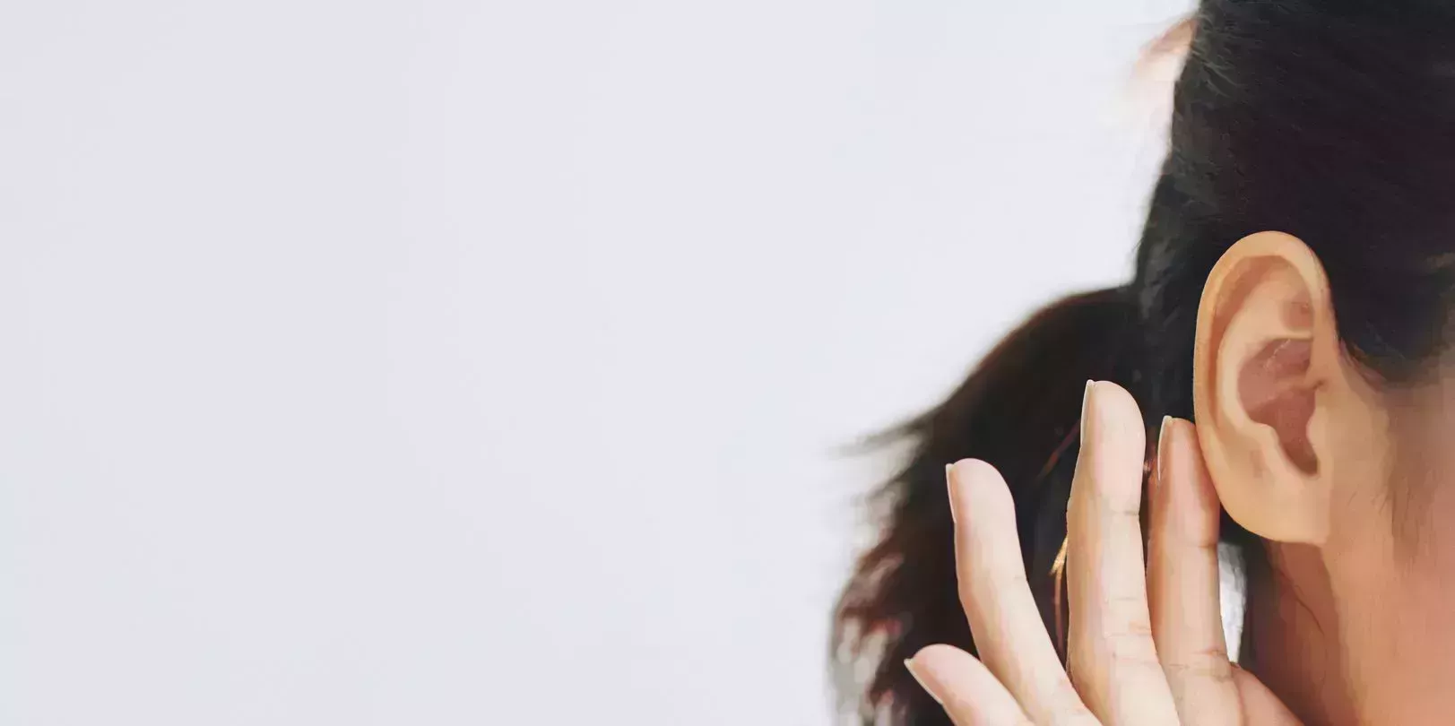 crop female with dark hair in ponytail touchingear with help of fingers and with tenderness on grey background