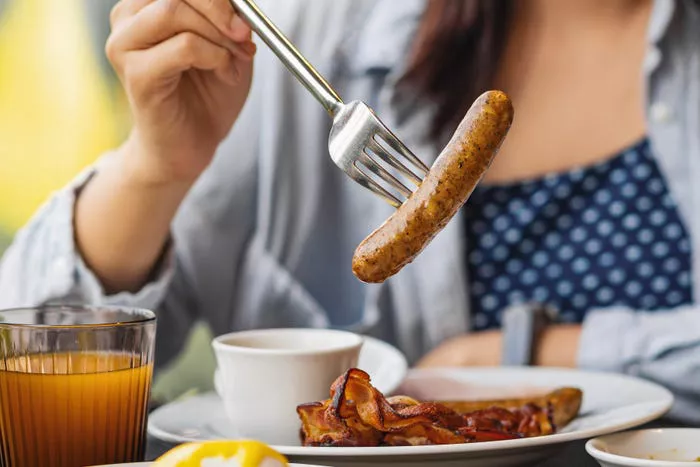 una mujer comiendo bacon y salchichas en el desayuno