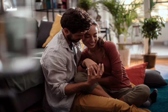 Joven pareja sentada junta en el suelo y tomados de la mano.
