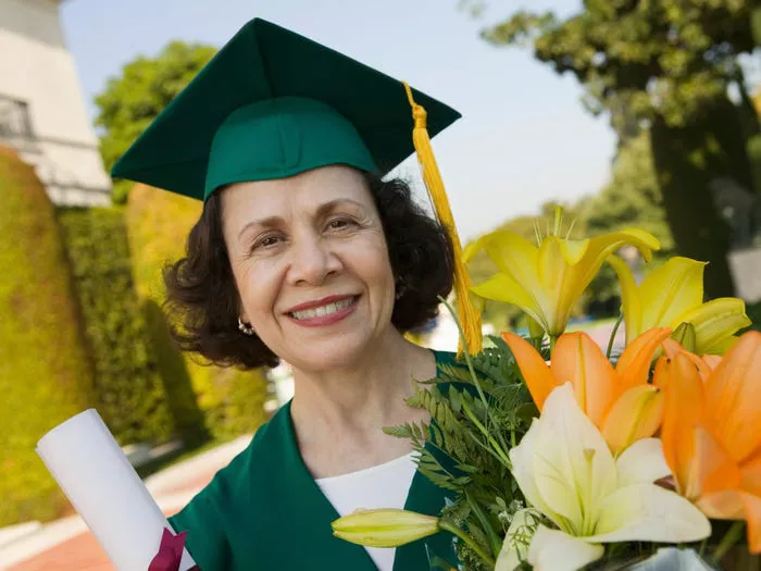 una mujer mayor con un sombrero de graduación y sosteniendo flores