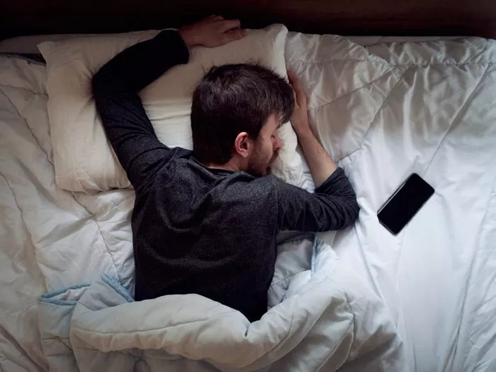 a man sleeping on his stomach in bed with an iPhone next to him