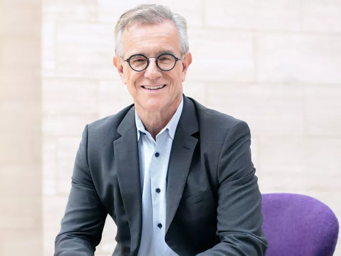 Eric Verdin sits on a purple chair wearing a suit.