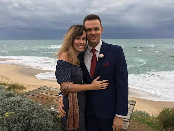 La autora y su esposo vistiéndose de manera formal y de pie cerca de una playa.